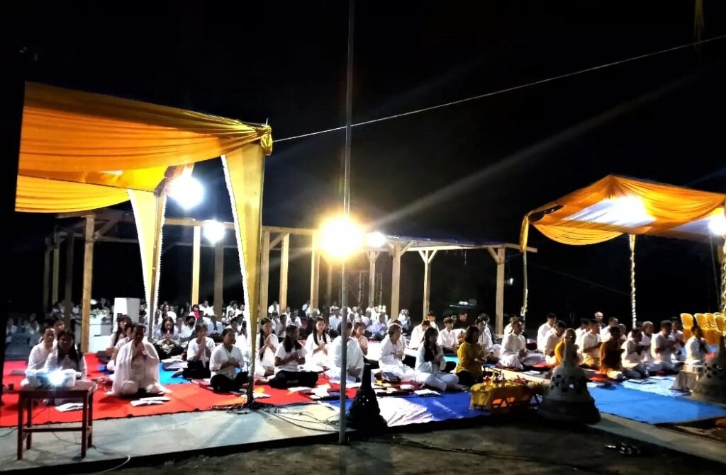 Sekelompok orang duduk di bawah tenda pada malam hari.