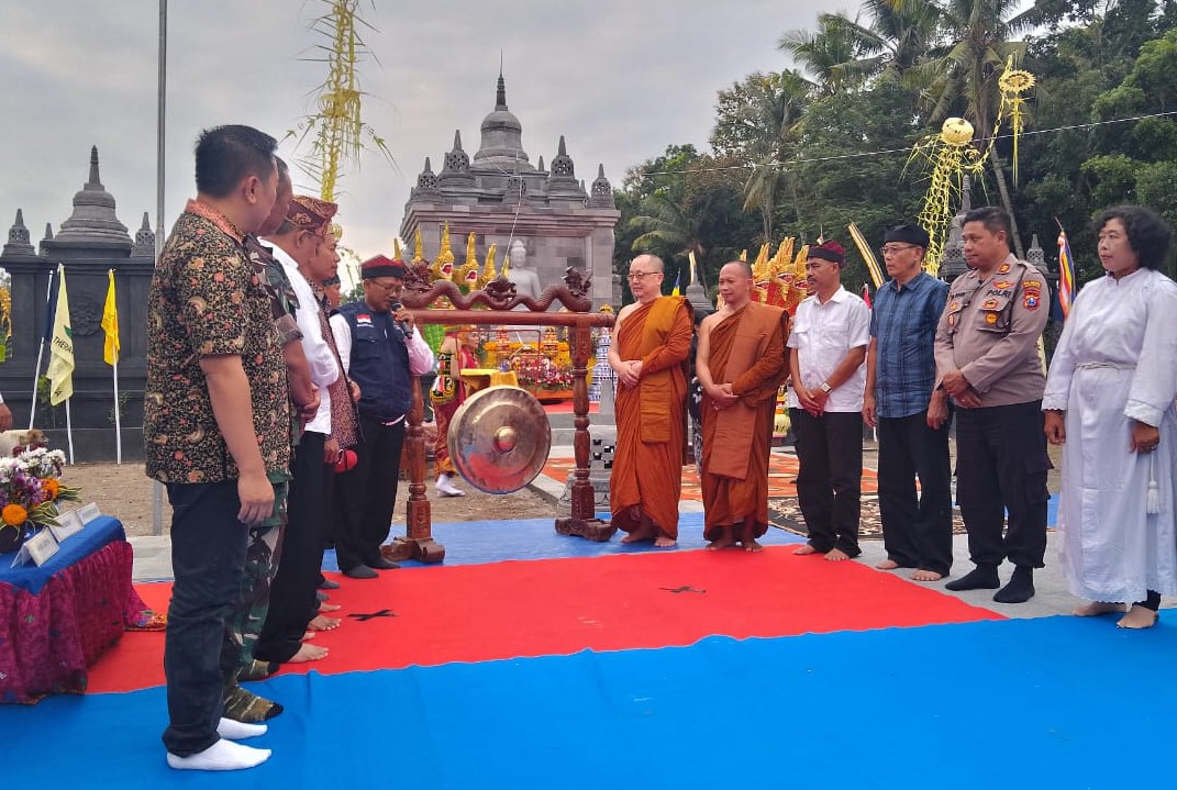 Sekelompok orang berdiri di depan patung biksu Buddha.